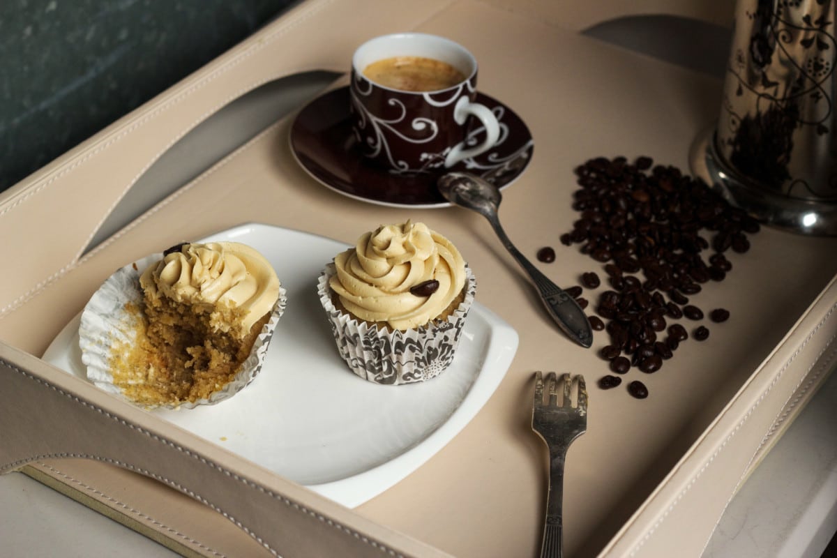 two cupcakes on white plate, espresso cup and scattered coffee beans
