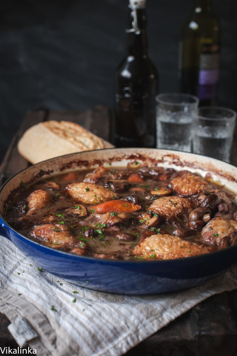 Chicken coq au vin with red wine and glasses in background