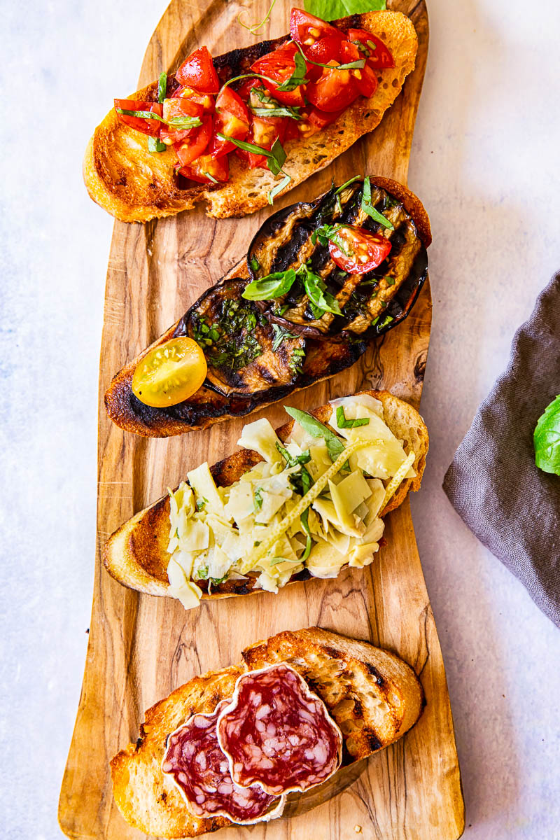 Four bruschetta slice with various toppings on wooden board. 