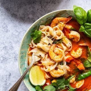 top down view of red curry with shrimp and rice noodles in a blue bowl