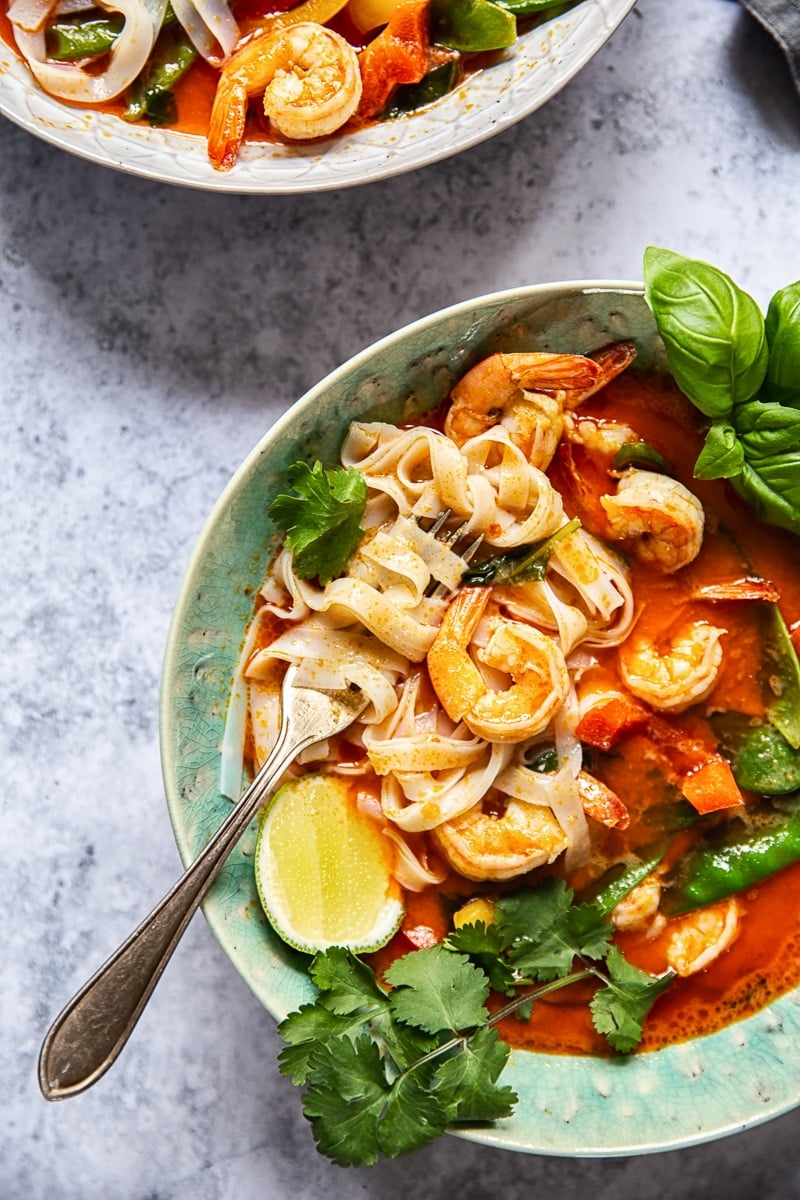 top down view of red curry with shrimp and rice noodles in a blue bowl 