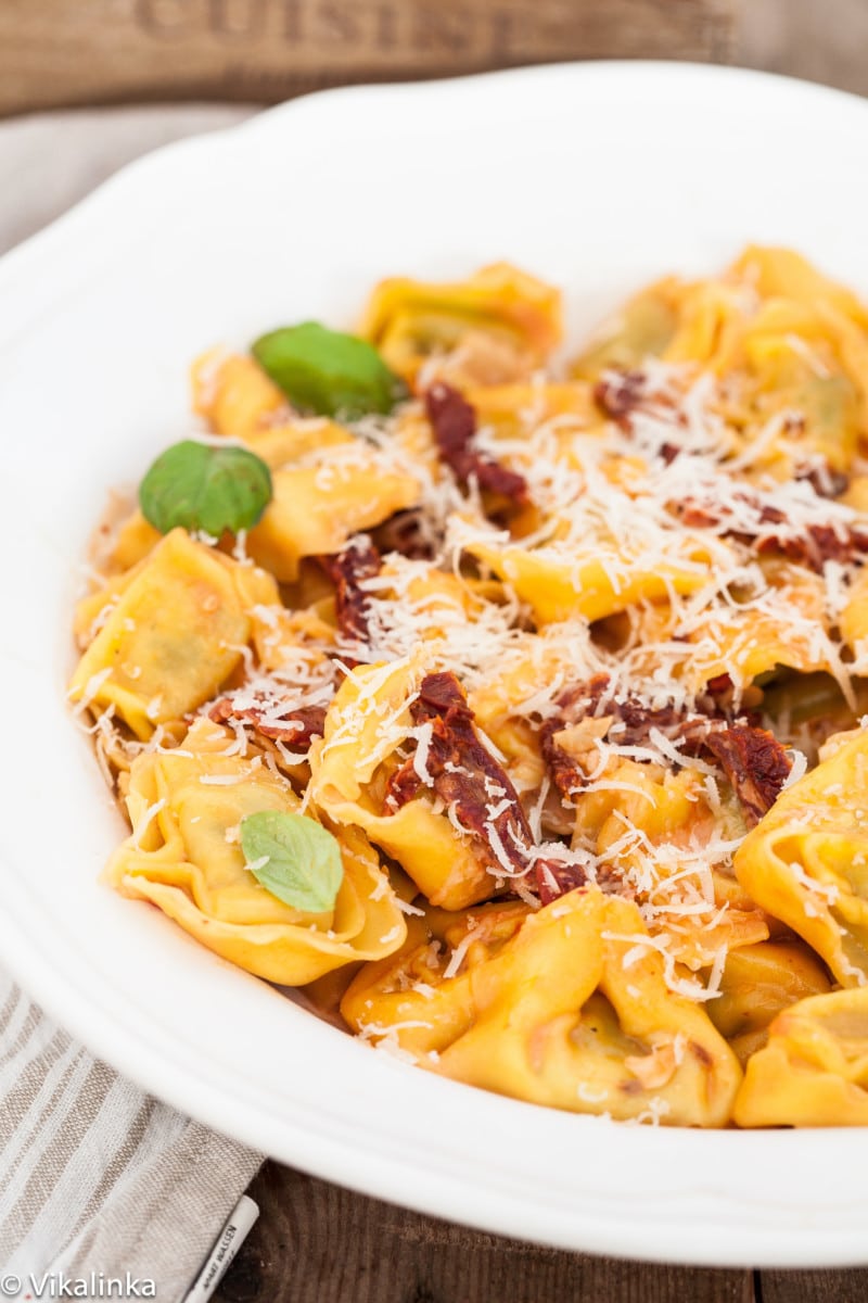 tortellini with orange sauce and sun-dried tomatoes in a white bowl