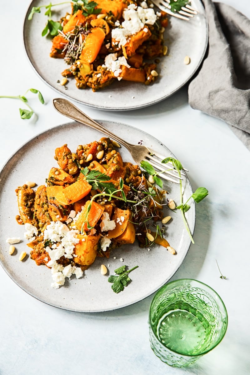 top down view of two grey plates with butternut squash and lentils, green glass