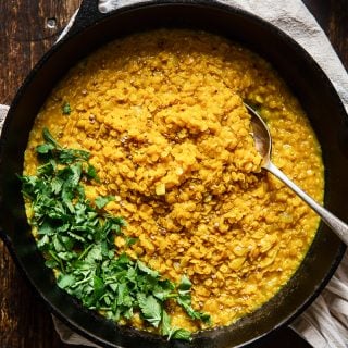 Top down of a pan of red lentil dahl on a wooden surface with parsley on top