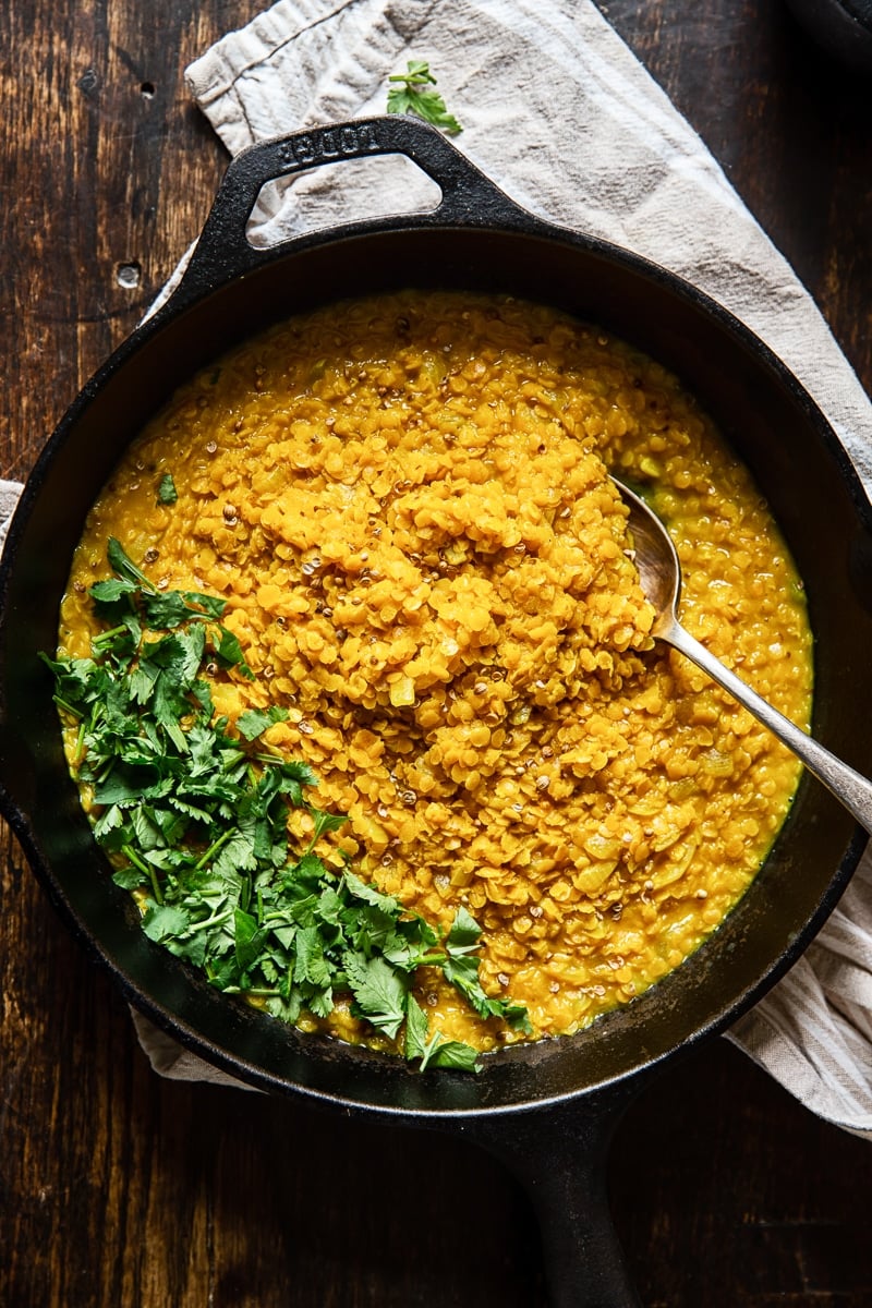 Top down of a pan of red lentil dahl on a wooden surface with parsley on top