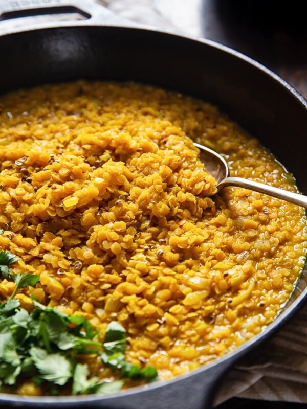 Close up of a cast iron pan showing red lentil dahl with a spoon