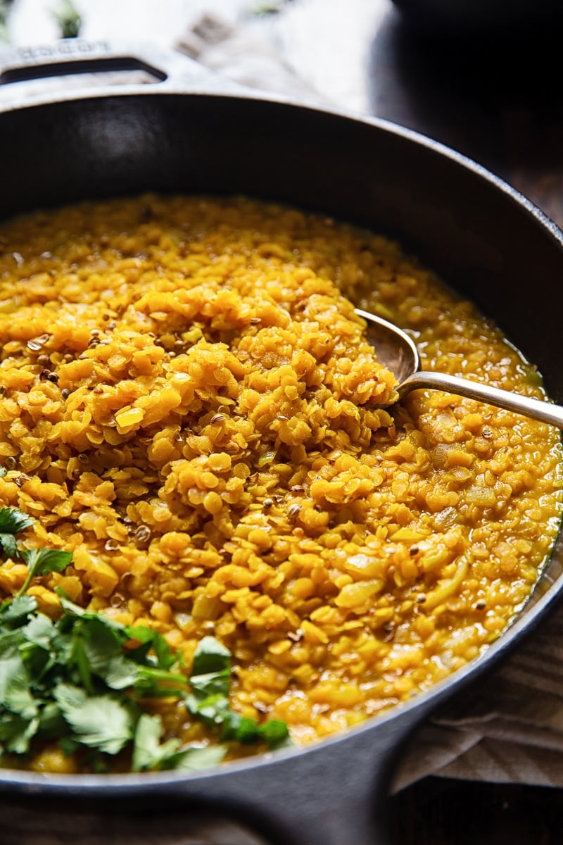 Close up of a cast iron pan showing red lentil dahl with a spoon