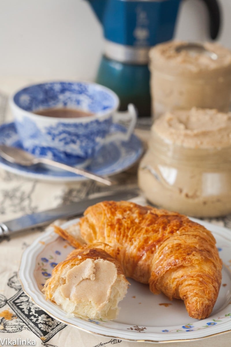 cashew butter on a croissant, a cup of coffee and a jar of cashew butter in the background