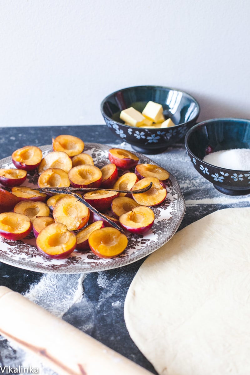 plums cut in half on plate, puff pastry rolled out and bowl of sugar and cubed butter