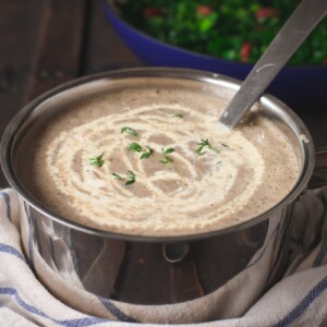 Mushroom soup in a pot with cream drizzled on top of it.