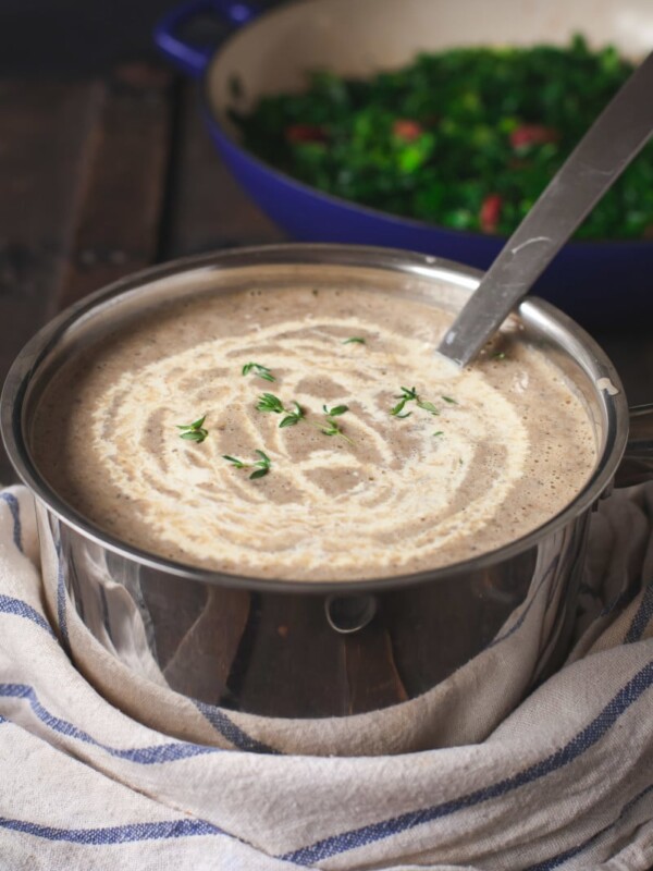 Mushroom soup in a pot with cream drizzled on top of it.