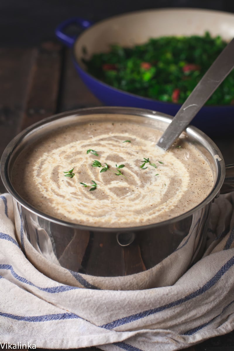Mushroom soup in a pot with cream drizzled on top of it.