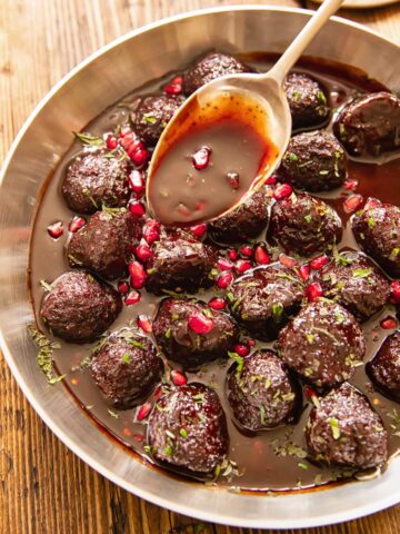 Pan of meatballs with spoon drizzling pomegranate sauce