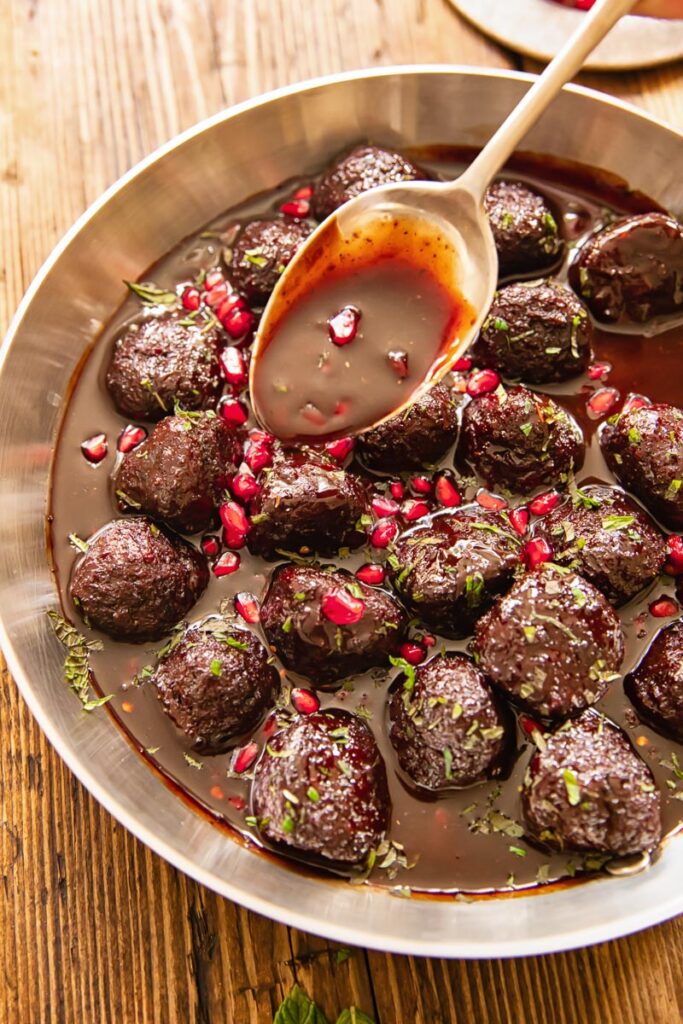 Pan of meatballs with spoon drizzling pomegranate sauce