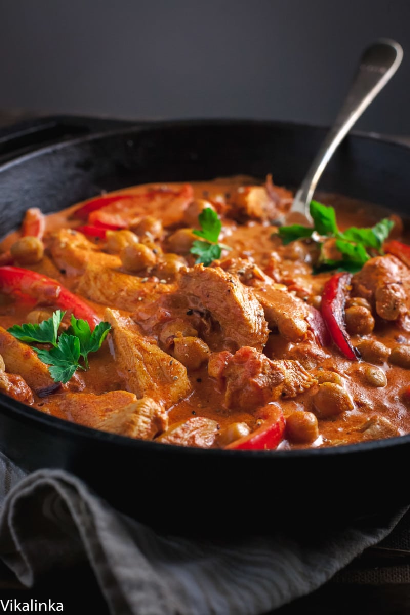 side view of chicken in red sauce with red peppers in cast iron skillet