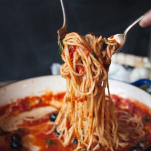 spaghetti with tomato sauce being tossed in a blue pan