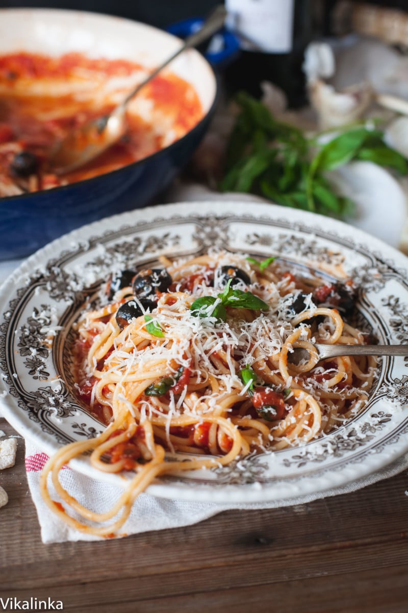 a bowl with spaghetti and black olives topped with parmesan cheese