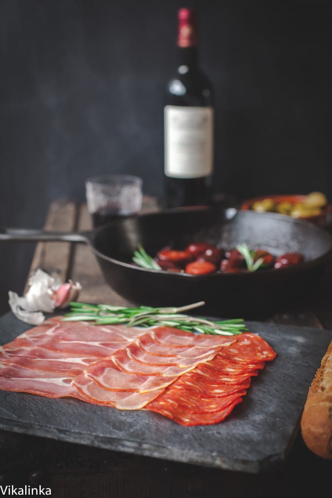 Tapas with cured meat in the foreground and wine behind