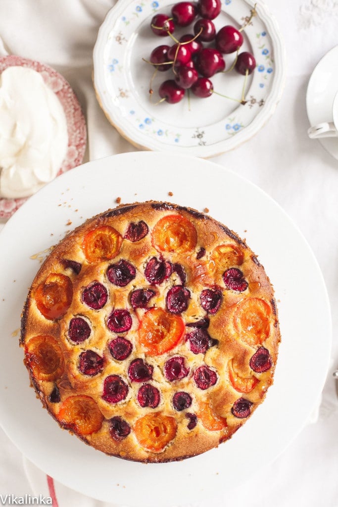 Cake on platter beside plate of cherries