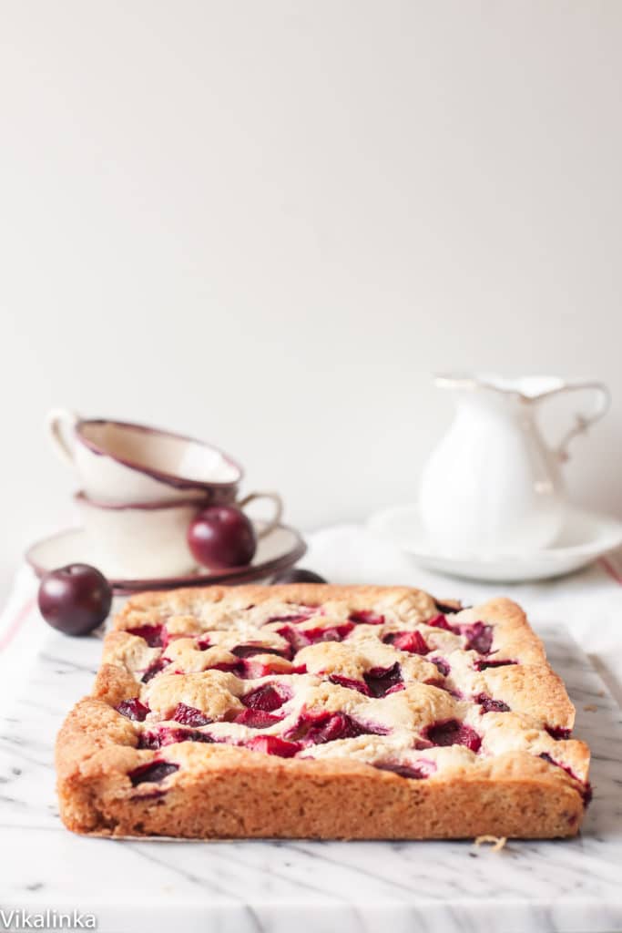 Side view of baked rustic plum cheesecake with tea set in the background