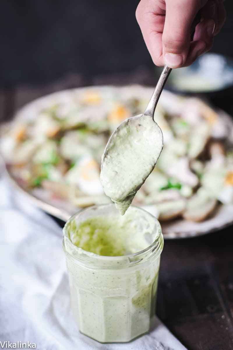 Jar of green goddess dressing with a spoon and potatoes in the background