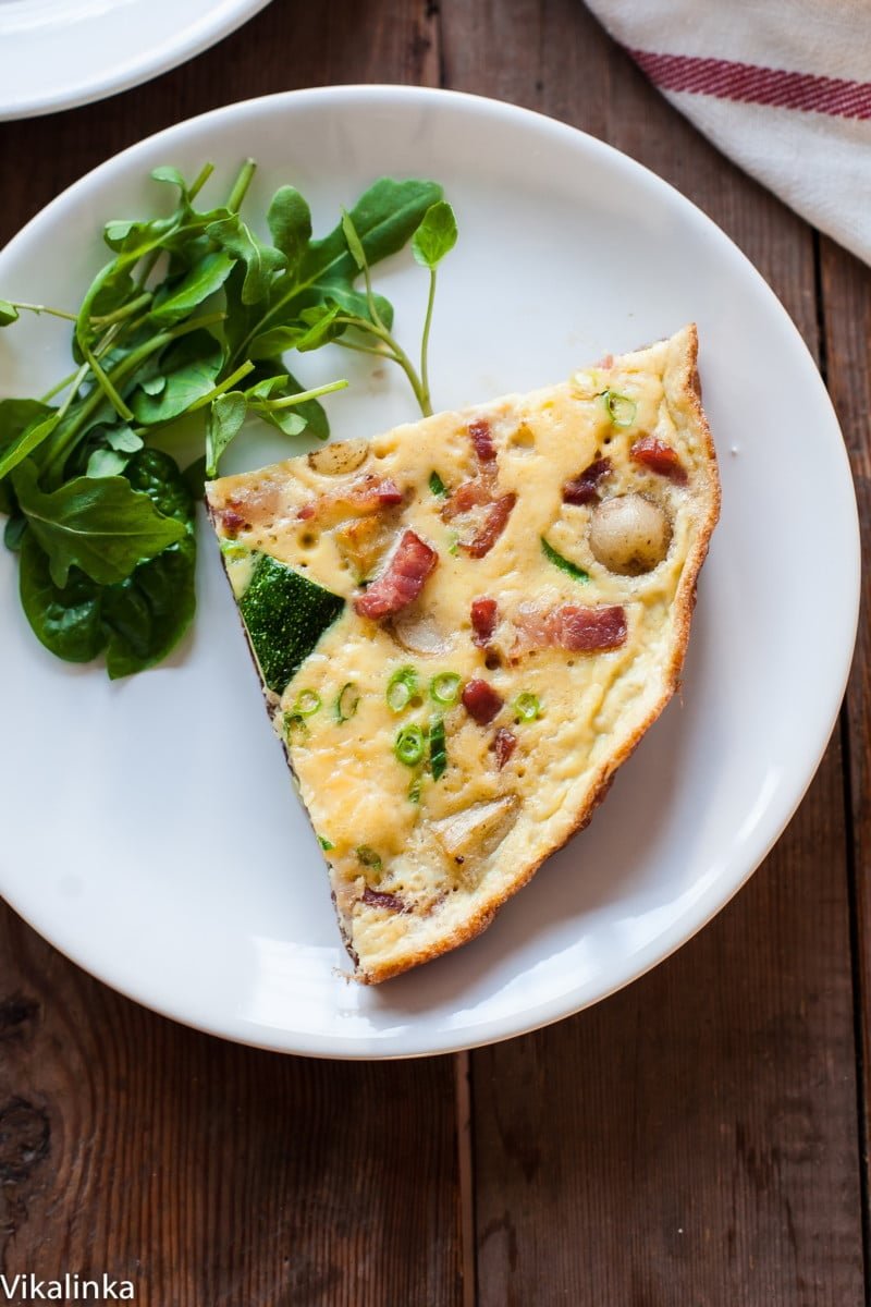 a slice of French omelette with a side salad on white plate