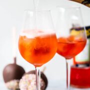 Bottle of sparking wine pouring into a glass with orange drink