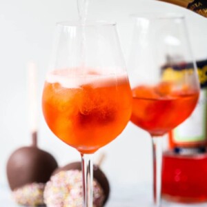 Bottle of sparking wine pouring into a glass with orange drink