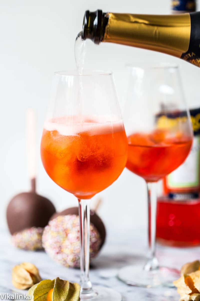 Bottle of sparking wine pouring into a glass with orange drink