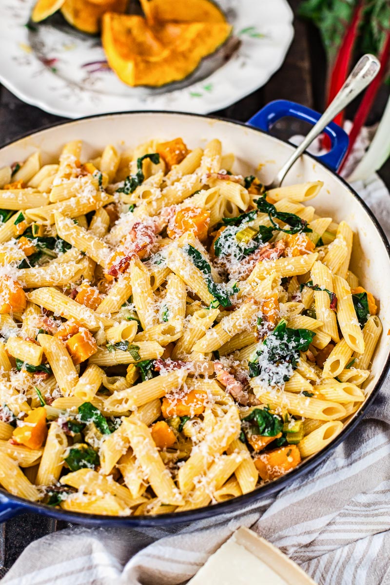 penne pasta with squash and bacon in a pan, roasted squash in the background