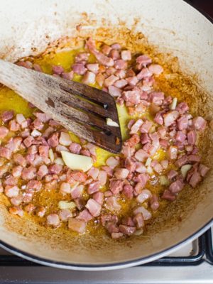 Wooden spatula mixing bacon in pan