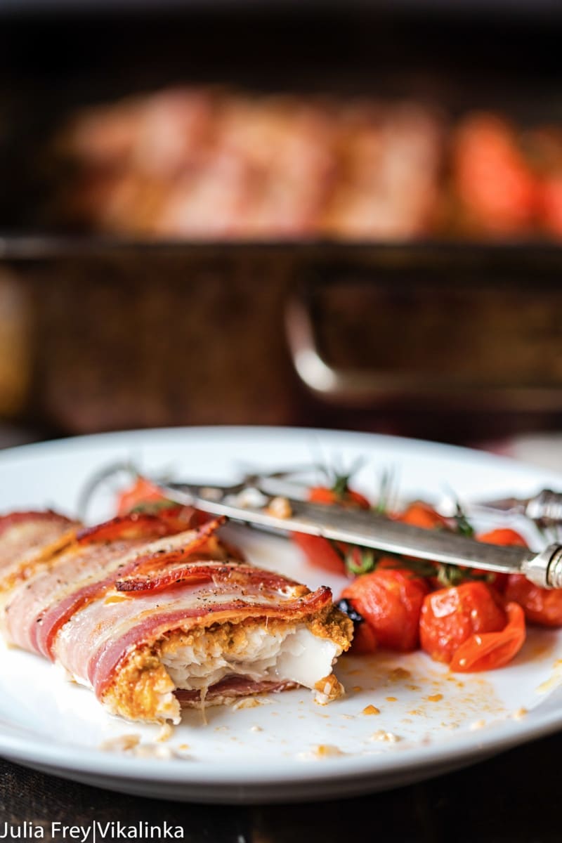 bacon wrapped white fish with roasted cherry tomatoes on white plate