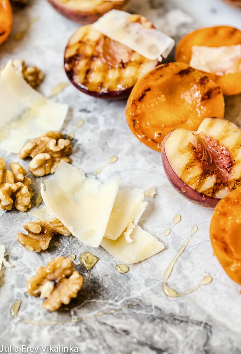 Close view of grilled apricots and walnuts alongside walnuts and grano padano shavings