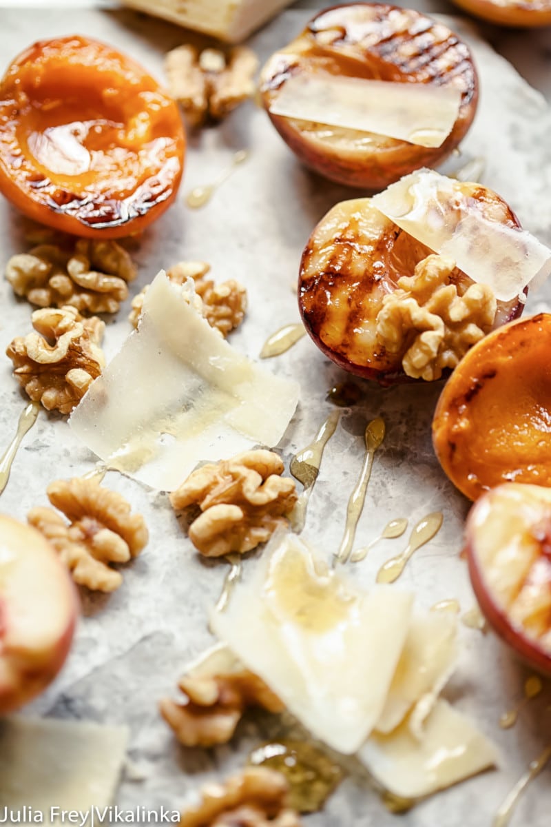 Close up of peaches and apricots along with cheese shavings, honey and walnuts