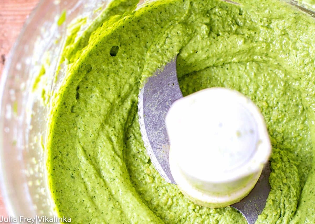 Close up of the inside of a food processor with green basil pesto