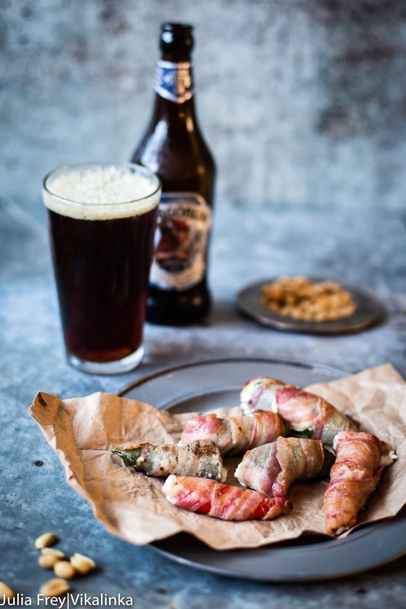 Bacon wrapped jalapeno poppers on a plate next to a beer
