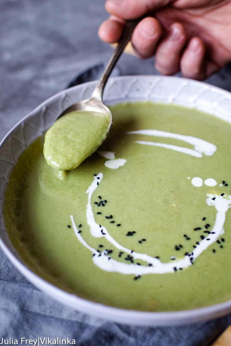 Cream of Broccoli in grey bowl, a hand holding a spoonful of soup over it
