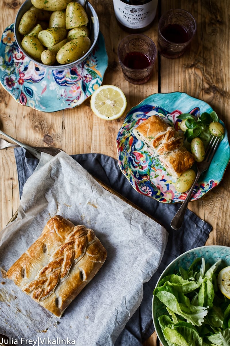 Top down view of salmon wellington. A blue plate with a slice of salmon, a bowl with baby potatoes and green salad