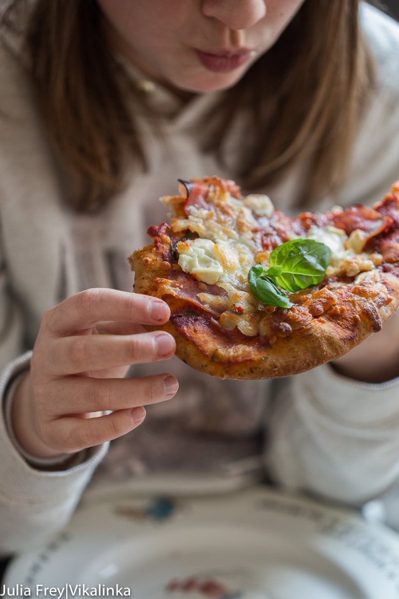 Girl eating a slice of pizza with a piece of basil showing clearly