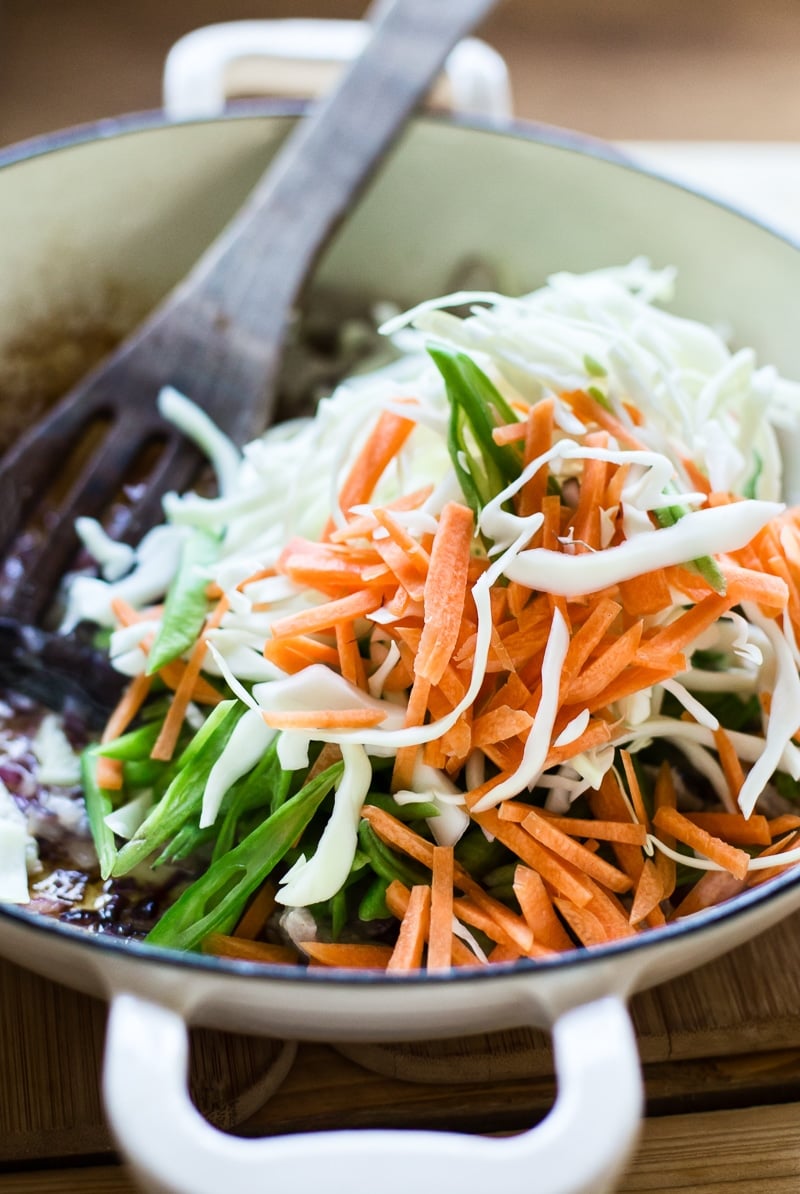 sliced cabbage, carrots and green beans in pan. 