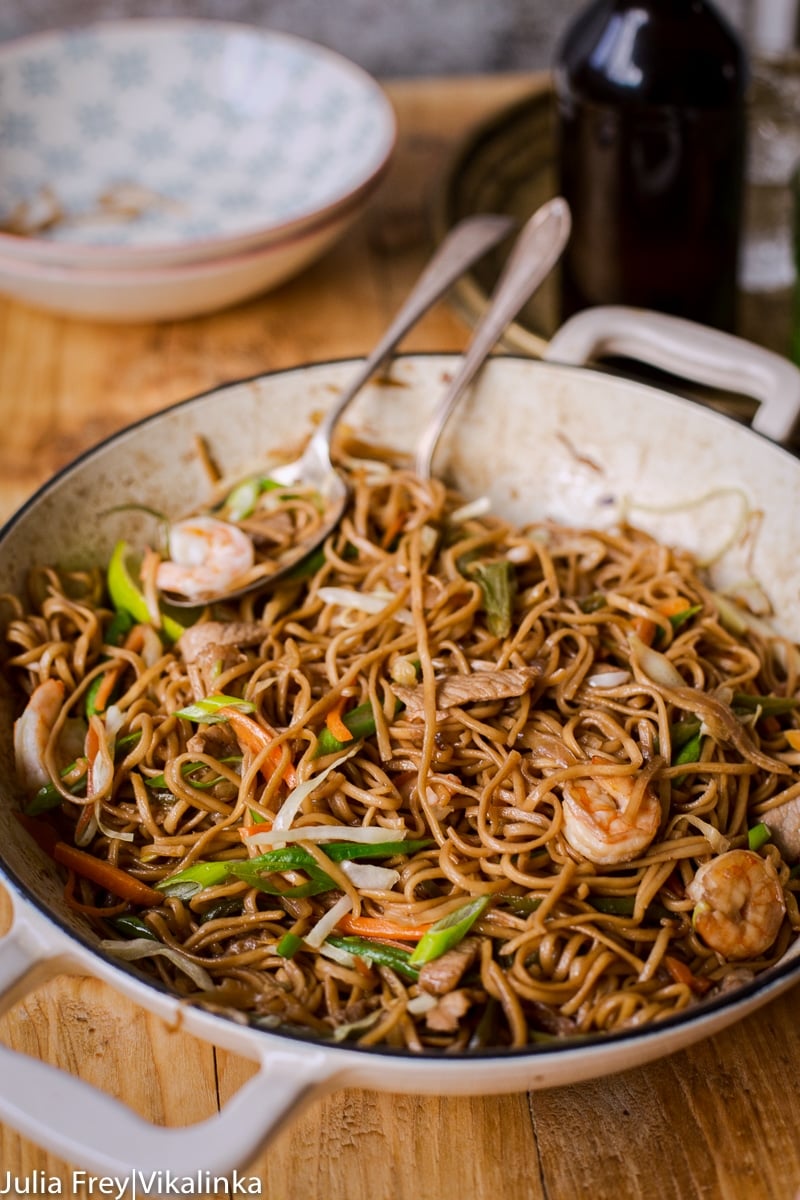 noodles with shrimp and vegetables in a while pan, bowls in the background