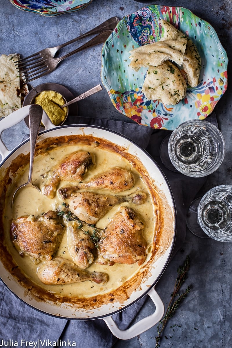 chicken in sauce in white pan, two wine glasses and a plate with torn bread pieces.