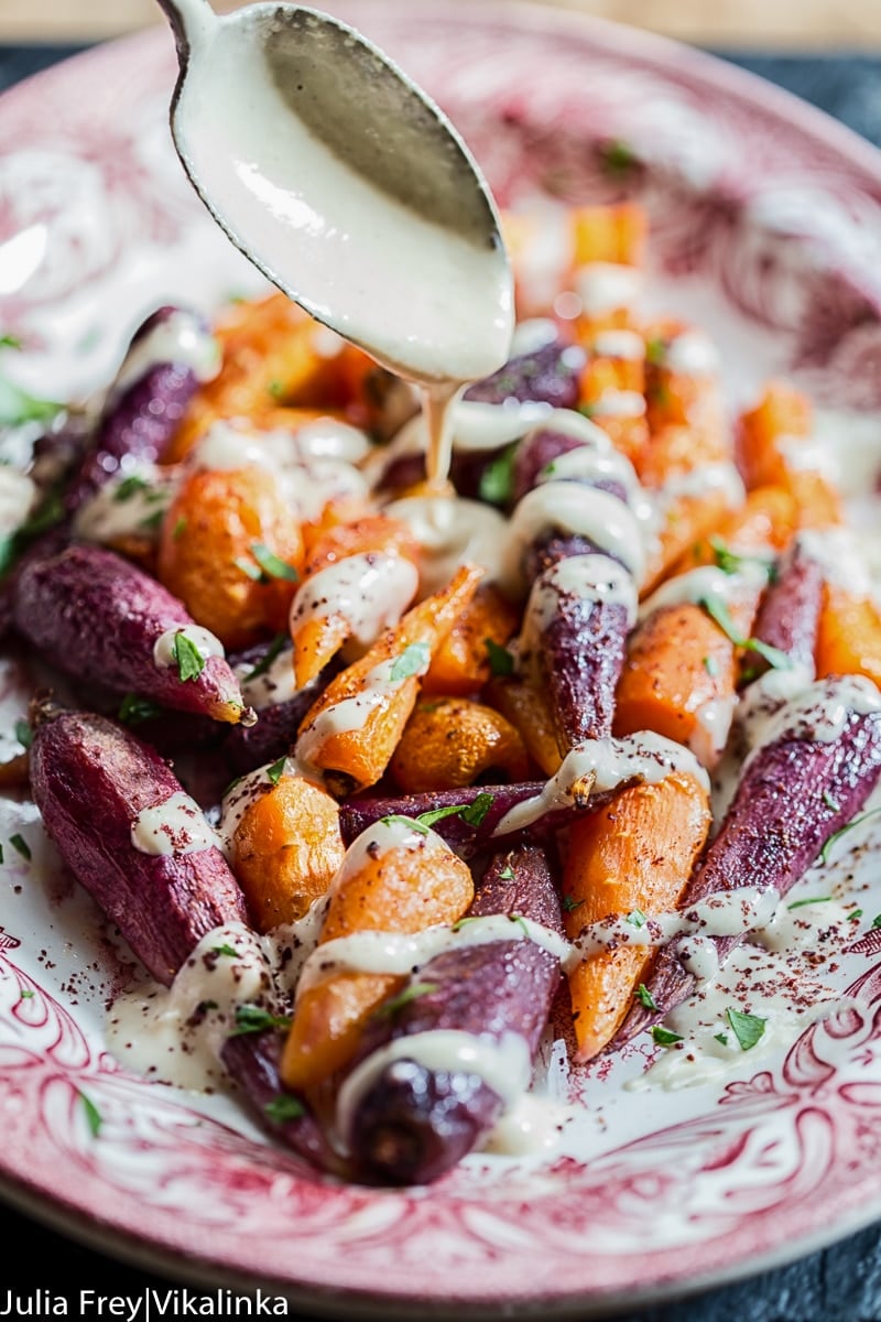 spoon pouring tahini sauce over roasted carrots