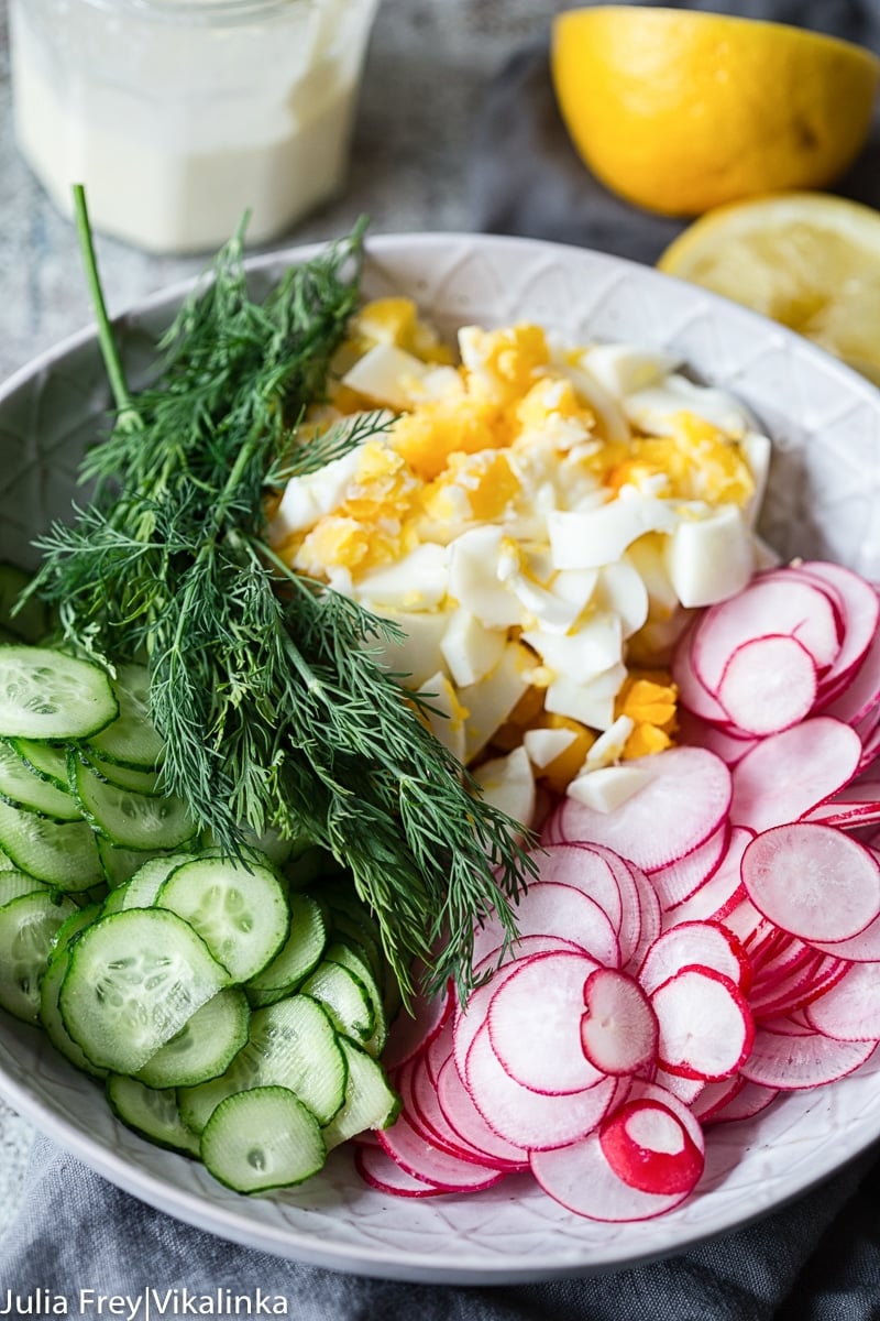 sliced cucumbers, radishes, chopped hard boiled eggs and fresh dill in a bowl, lemon in the background.