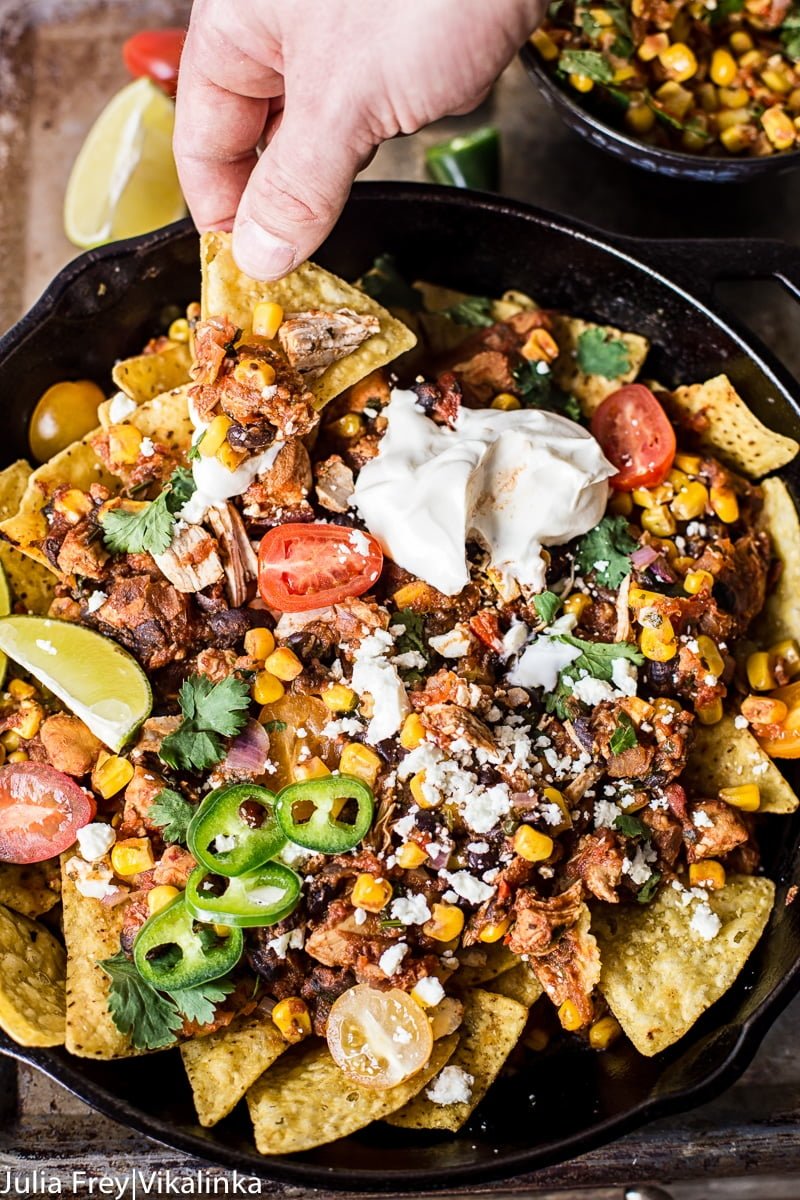 Hand pulling nacho from the Chicken Chilaquiles