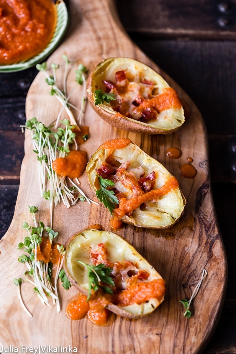 Three potato skins with chorizo and bravas sauce on a wooded platter