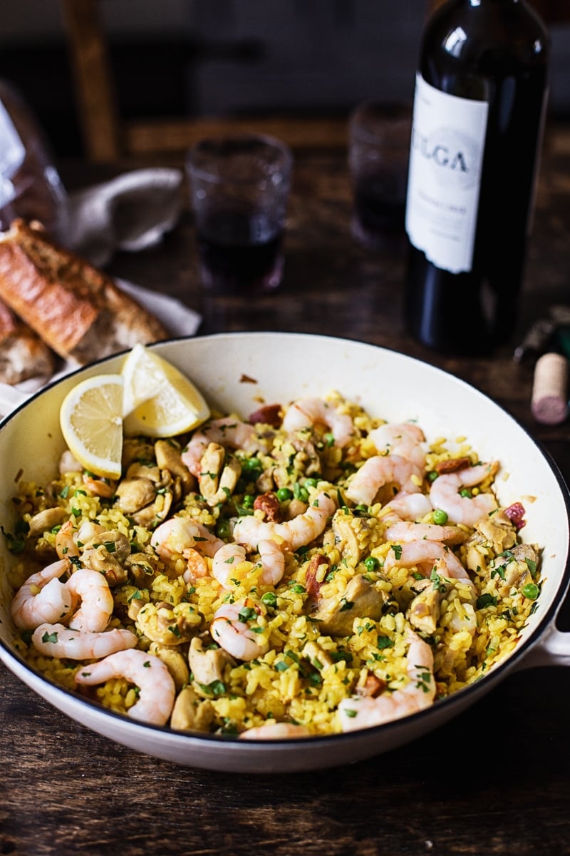 Spanish rice with shrimp in a while pan, baguette and wine in the background