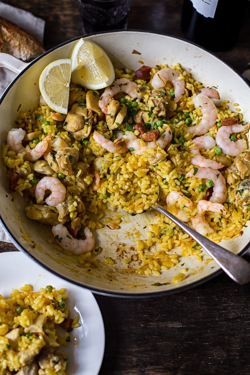 Spanish rice in a while pan with a spoon in it, a small white plate filled with the dish next to it.