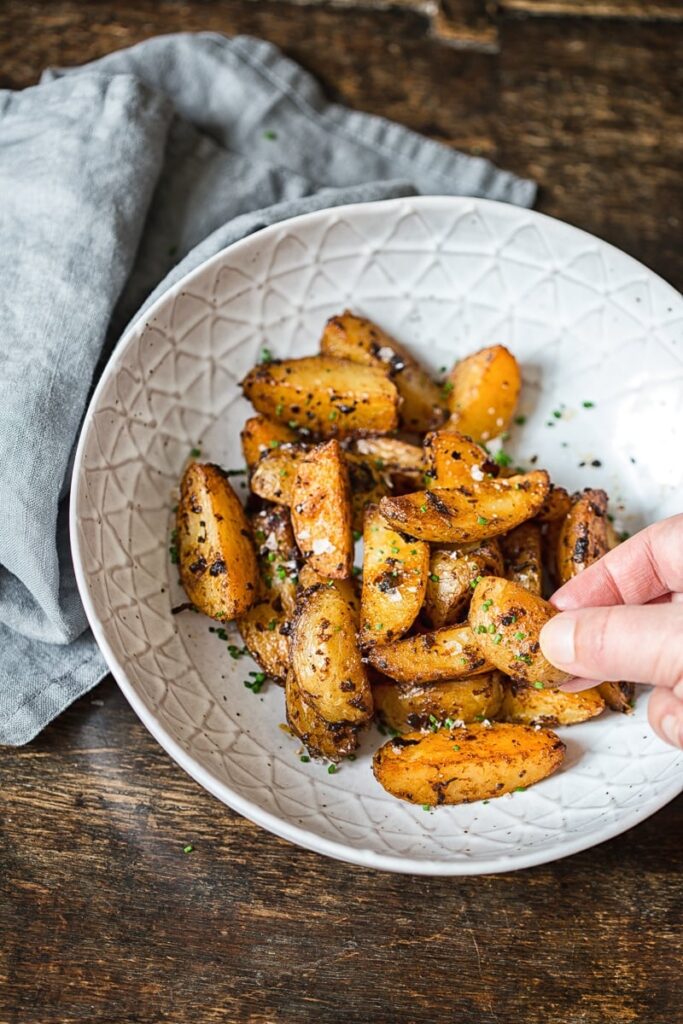 hand grabbing a potato wedge from a bowl