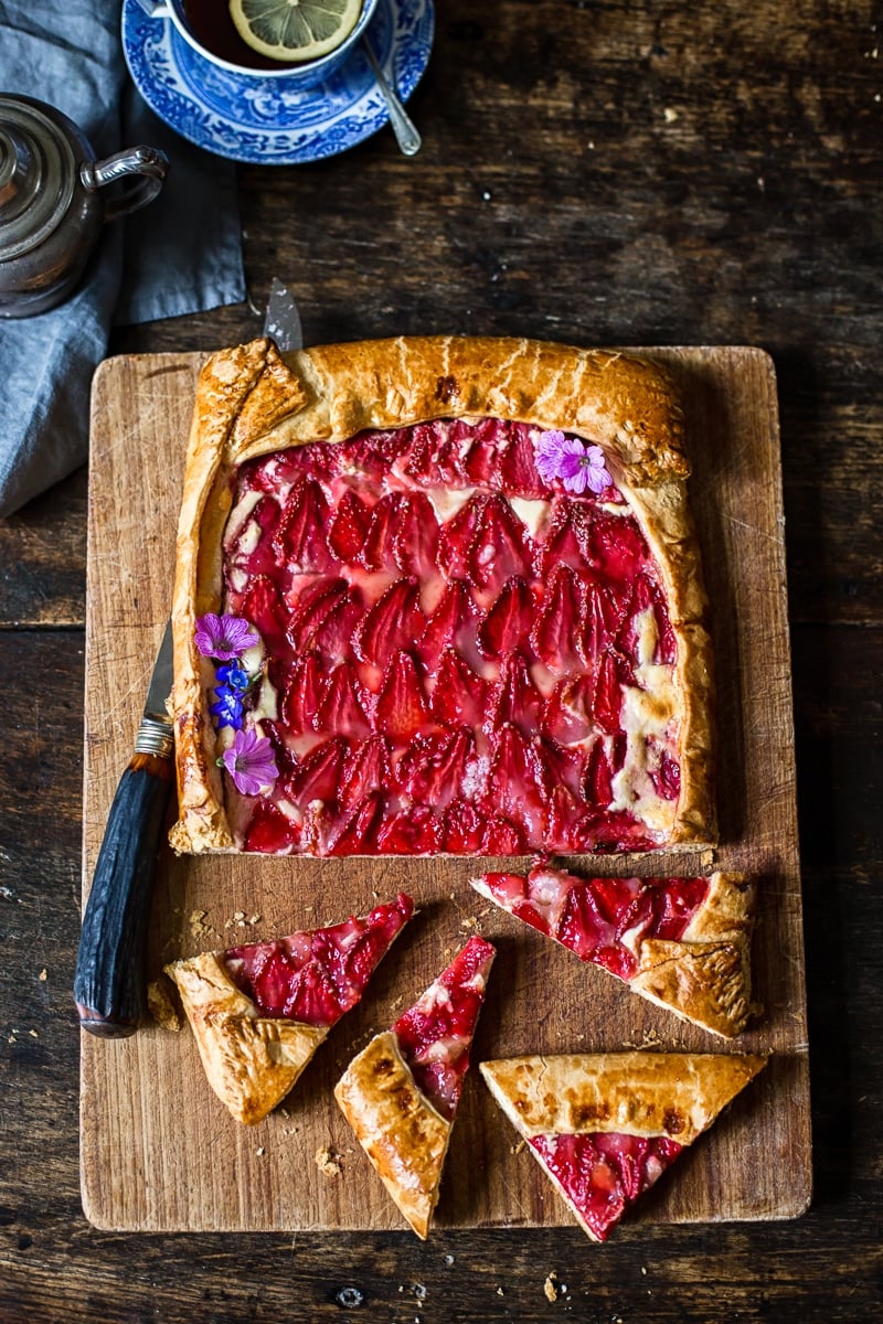 Top down view of strawberry galette on a cutting board with four pieces cut and to the side